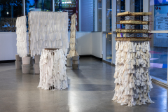 Three sculptures made from torn, white bedsheets tied to wire, stand on concrete supports in a gallery.