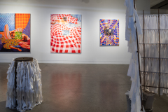 Three bright paintings hang on a white gallery wall. Each painting depicts a person surrounded by a checked motif. The focal point in each painting is obscured by a small square fragment.