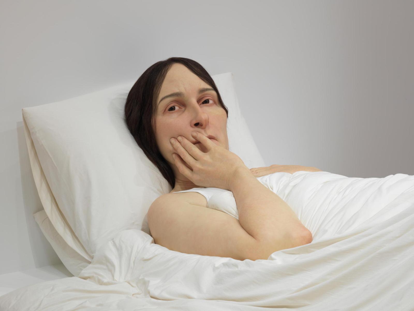 A sculpture shows a worried oversized woman lying in bed
