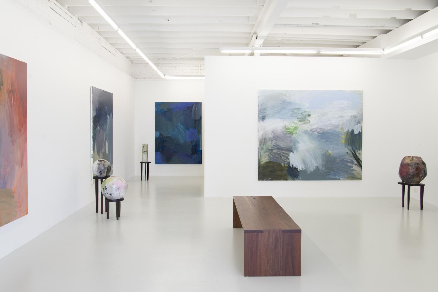 Large abstract canvases in cool and warm pastel colours fill a white gallery wall, small round sculptures sit on small black stools