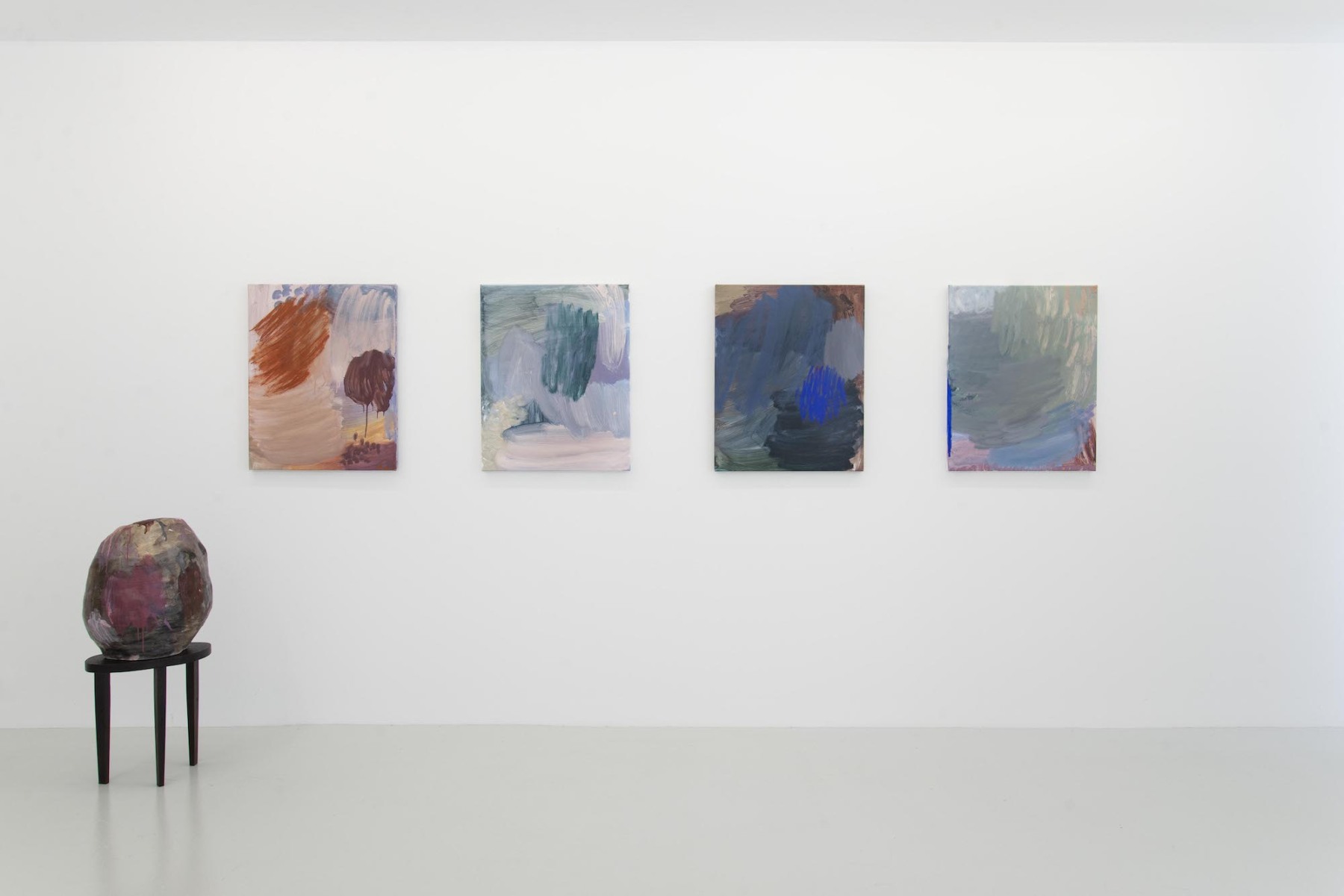 Four abstract canvases in cool and warm pastel colours hang on a white gallery wall, to the left one round sculpture sits on a small black stool