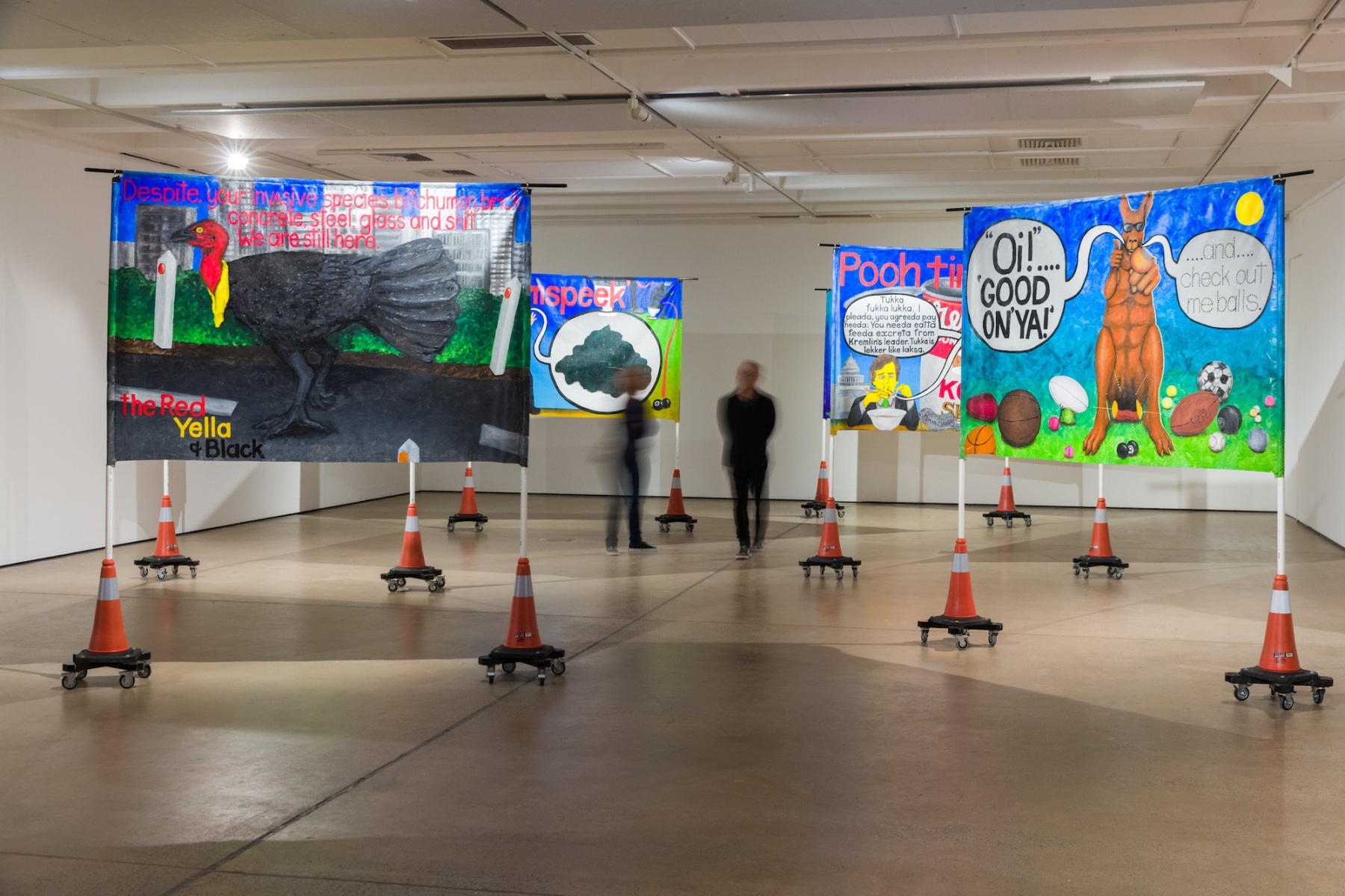 Painted banners, suspended between poles that are standing in traffic cones, fill the gallery