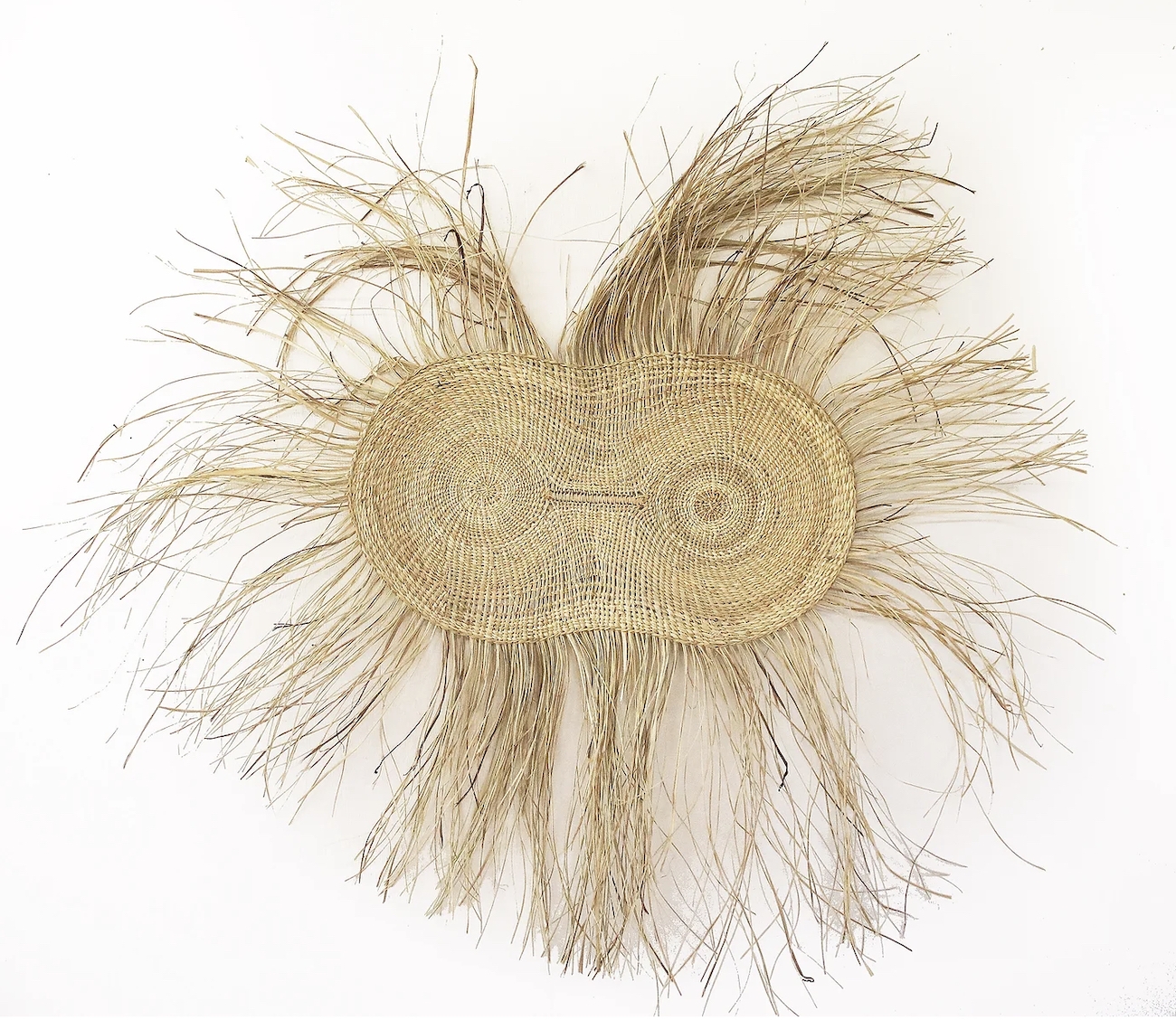 A pandanus weaving with two central circles hangs on a white wall