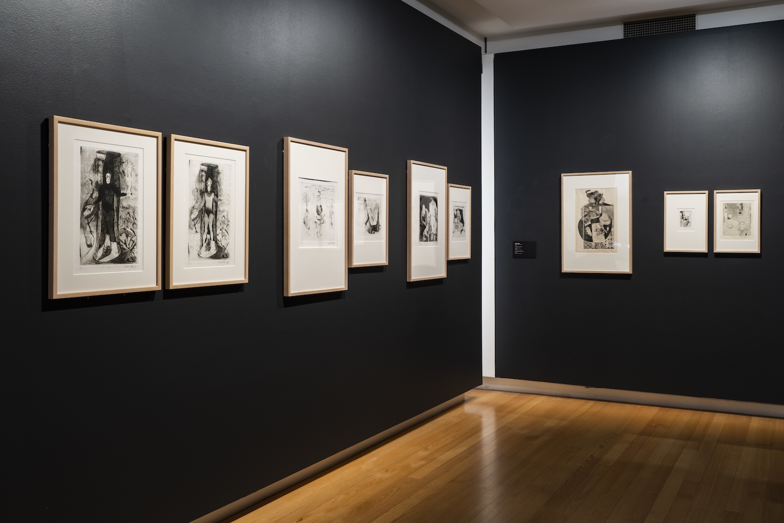 Black and white etchings framed in natural timber are installed on gallery walls painted black.