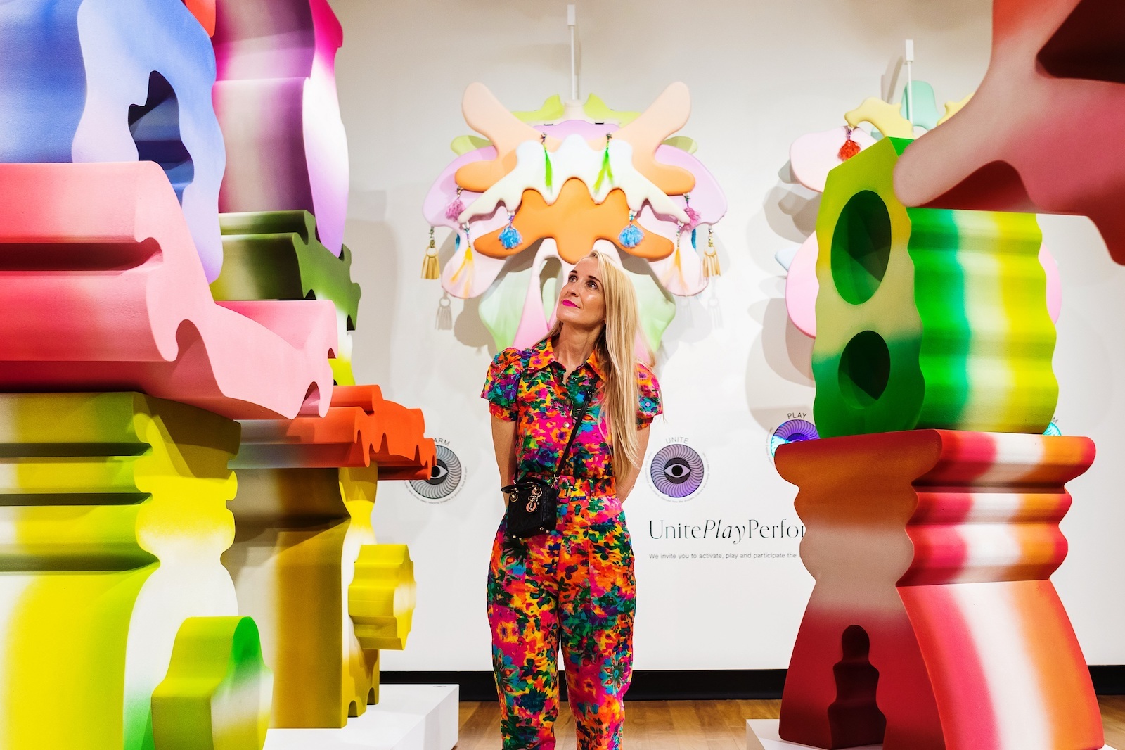 A woman stands among colourful foam shapes, soft layered sculptures hang from the wall
