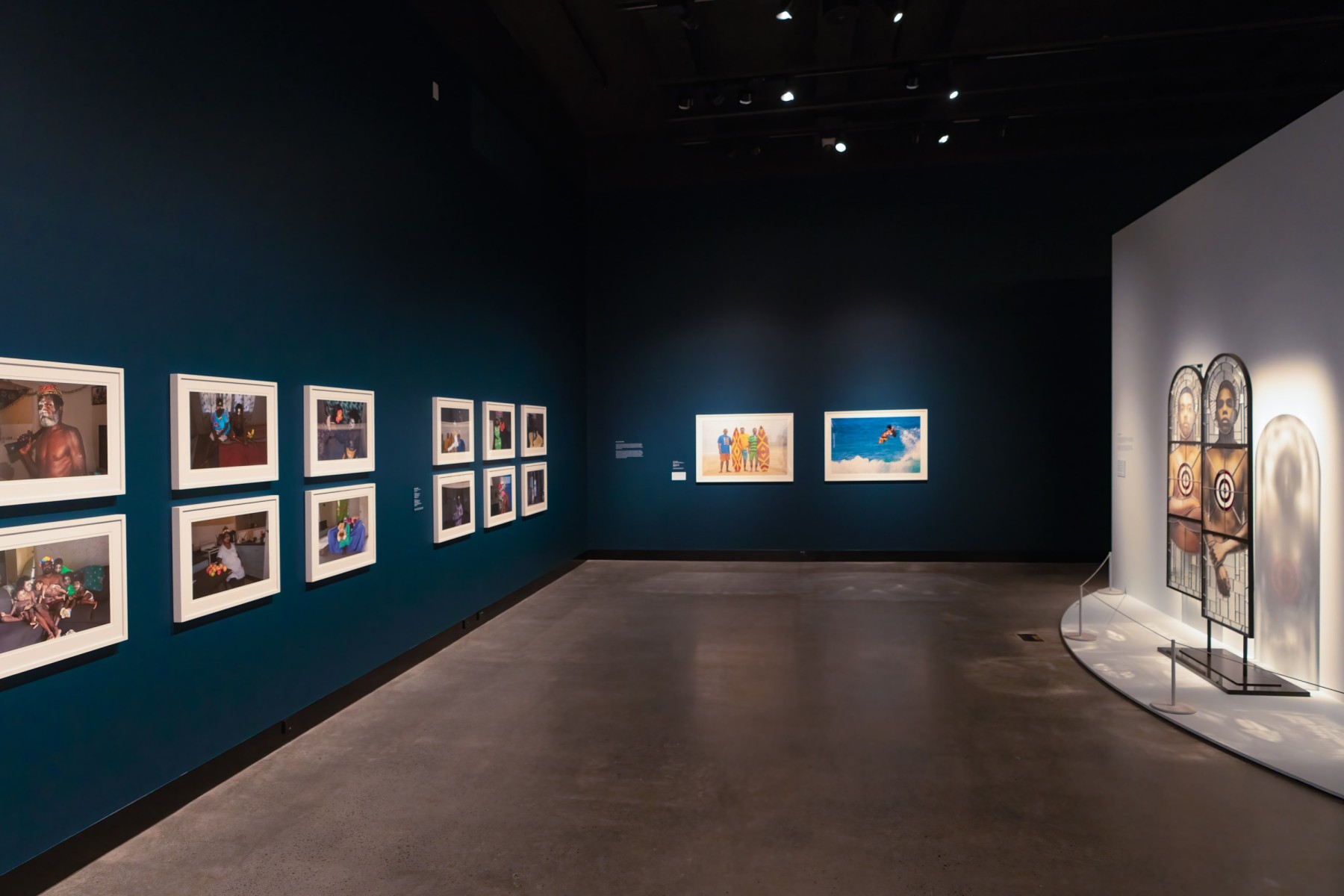 A gallery with darkened blue walls shows three series of photographic portrait works