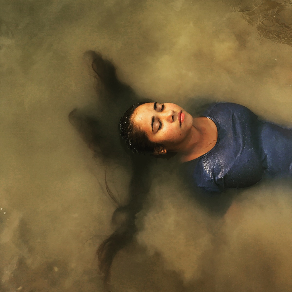 A woman with sprawling dark har closes her eyes and lies back in a river .
