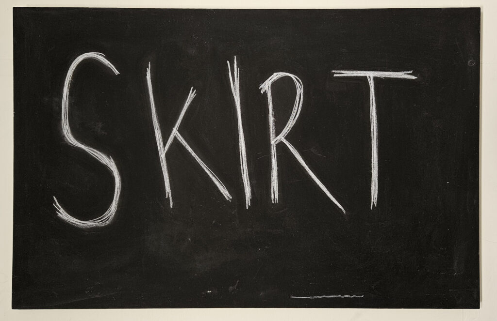 The capitalised word ‘skirt’ is written in sharp angular white chalk across a blackboard