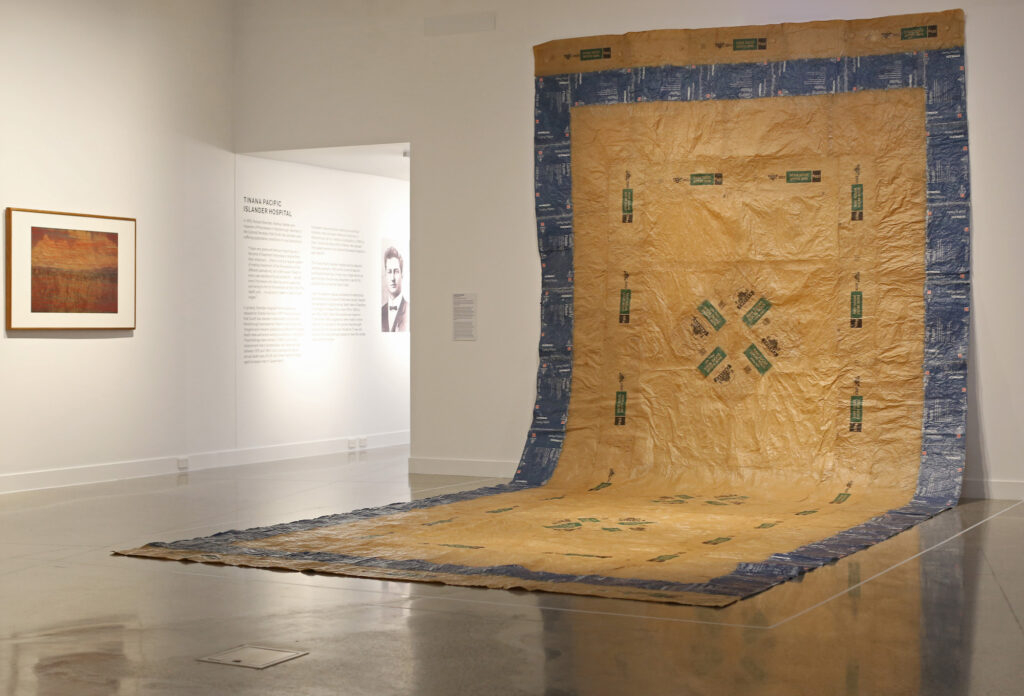 A barkcloth with blue and green patterns hangs from the gallery wall and spreads onto the floor. 