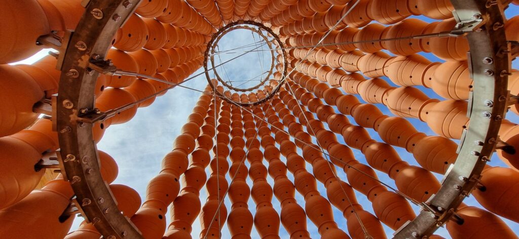 A photograph from inside an installation shows towering terracotta vessels against a blue sky