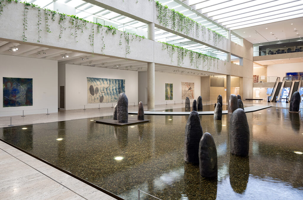 A large gallery with a water-feature floor shows multiple bronze sculptures like termite mounds.