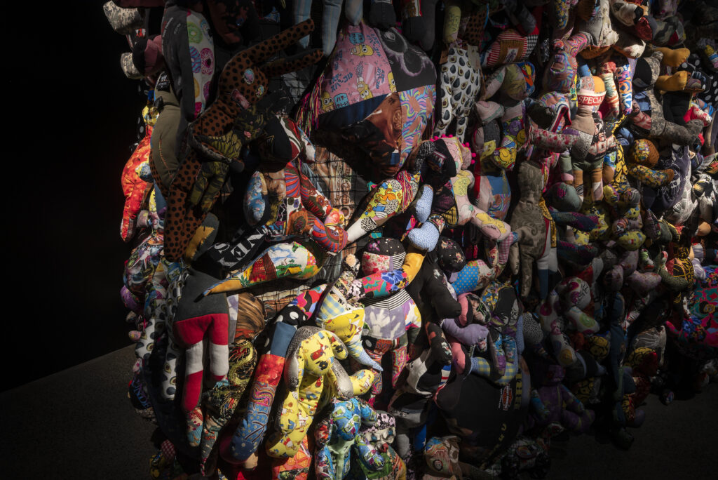 An image of a dimly lit wall displaying a mass of soft toy-like sculptures.