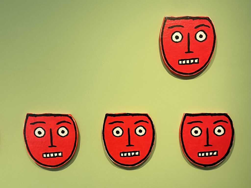 Four red, cartoonish faces float on a green background. 