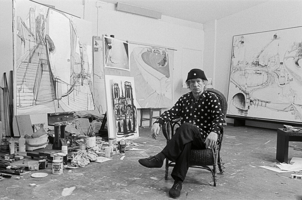 A black and white photograph of an artist sitting in his studio.