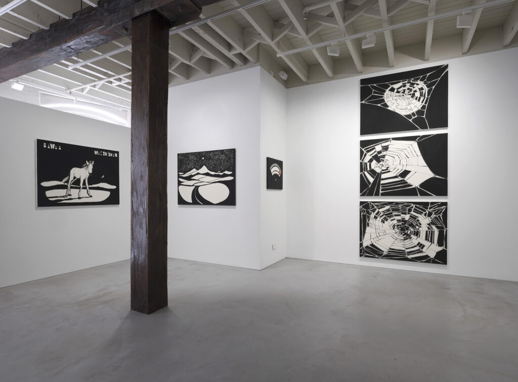 Black and white paintings in a gallery depict a donkey, a moonlit landscape, three spider webs and a gauge set to extreme.