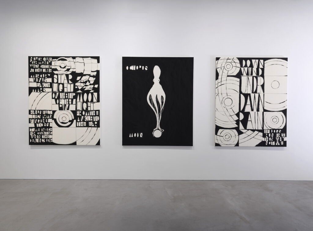 Three black and white paintings on a gallery wall. The other two merge large letters and abstract shapes, the middle depicts an elongated octopus-like form.