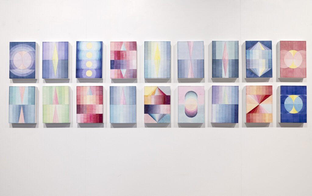 Two rows of delicate watercolour paintings with symmetrical geometric patterns hang on a gallery wall.