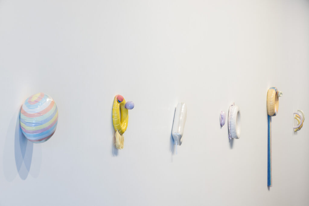 Colourful ceramic works are displayed hanging on a white gallery wall.