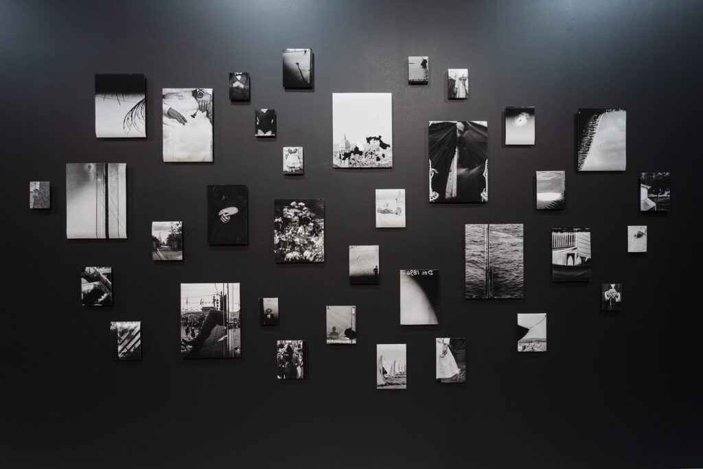 Fragments of black and white photographs hang across a darkened gallery wall.