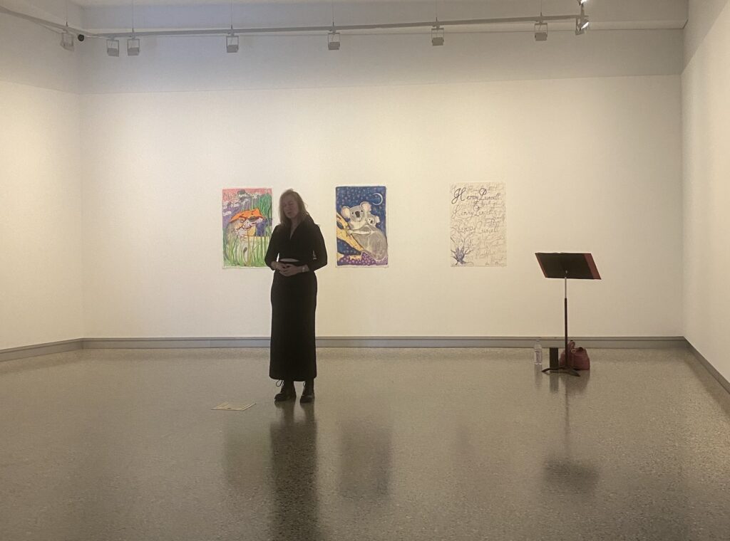 A woman wearing black sings with her eyes closed in a gallery; behind her are colourful illustrations of Australian fauna.