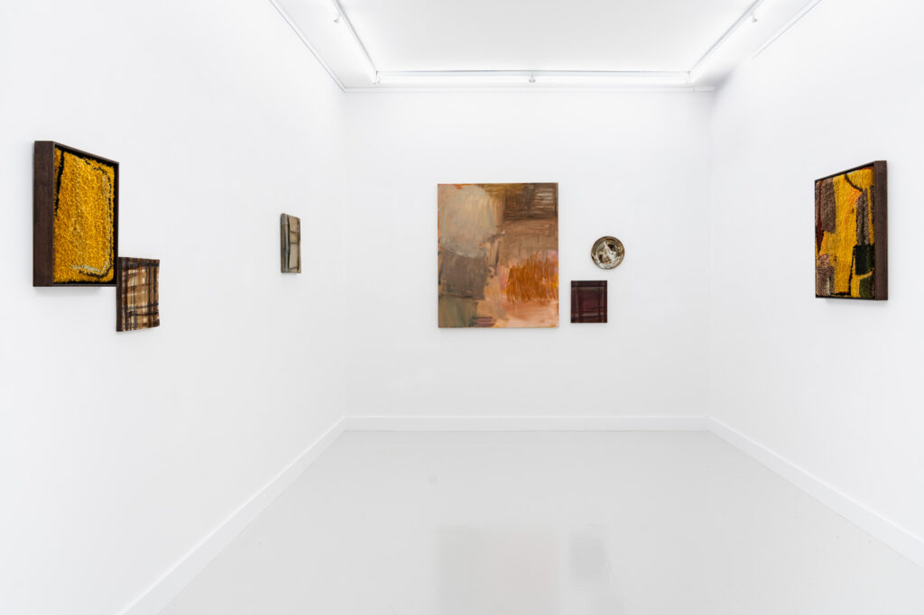 An interior of a gallery room shows abstract works in browns hanging on three white walls