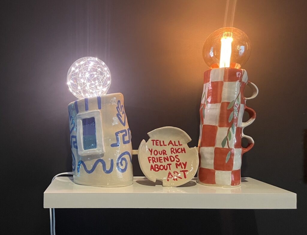 Ceramic clay sculptures, glazed and installed with functioning lightbulbs. Text reads ‘Tell all your rich friends about my art’.  