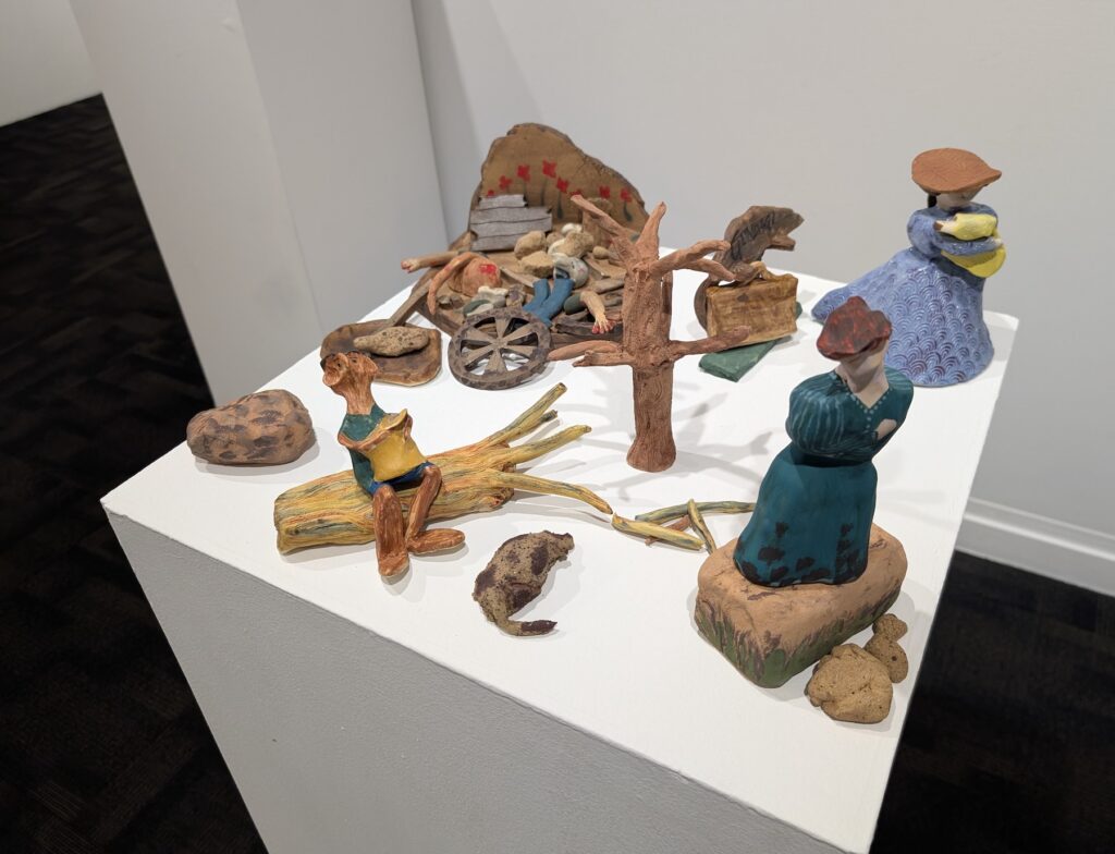 Ceramic figures sit on a white plinth, each depicting a moment in a story of hardship.