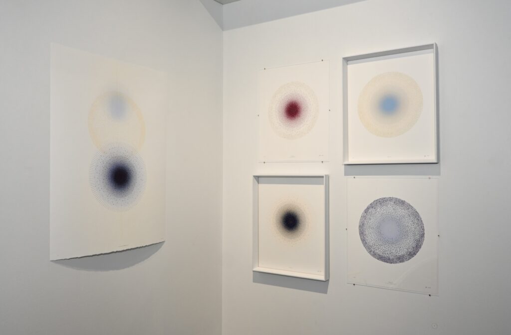 Five multilayer prints with a circular centre hang on two white gallery walls.