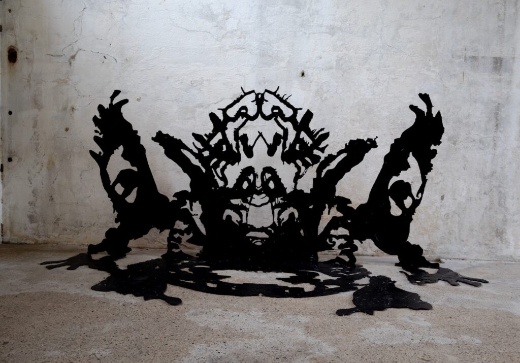 A black inkblot cut out folds into the corner of a concrete wall and floor.