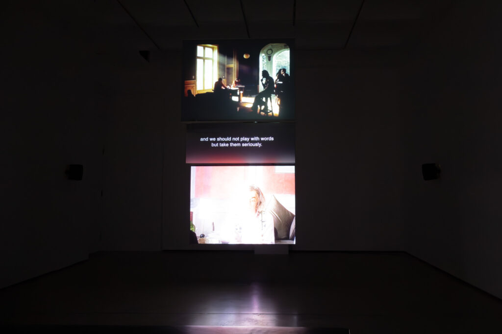Three screens stacked vertically in a dark room displaying collected clips, theoretical text, and interviews.