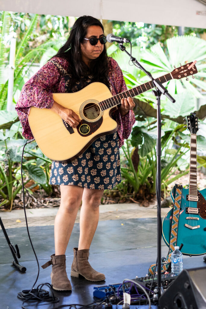 Jessie Chong-Grainer stands behind a microphone while holding an acoustic guitar