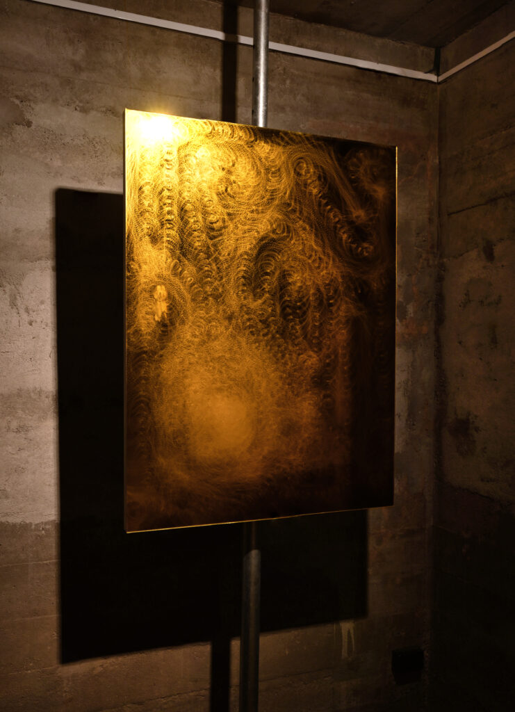 Large yellow rectangle reflecting golden light into the room around it. It is affixed in mid-air by being attached to one beam of grey metal scaffolding reaching floor to ceiling. The rectangle’s surface is made of yellow acrylic and is full of small swirling scuffs made by an angle grinder.