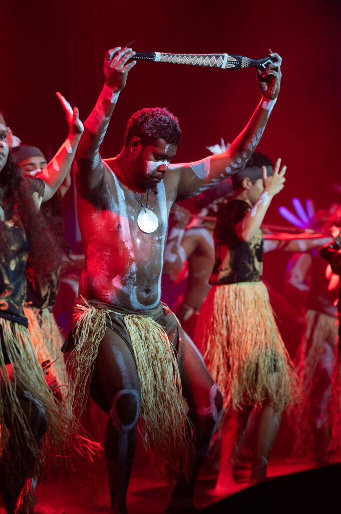 A group of Yidinji dancers in traditional attire perform at the CIAF Opening night beneath warm, red lights.