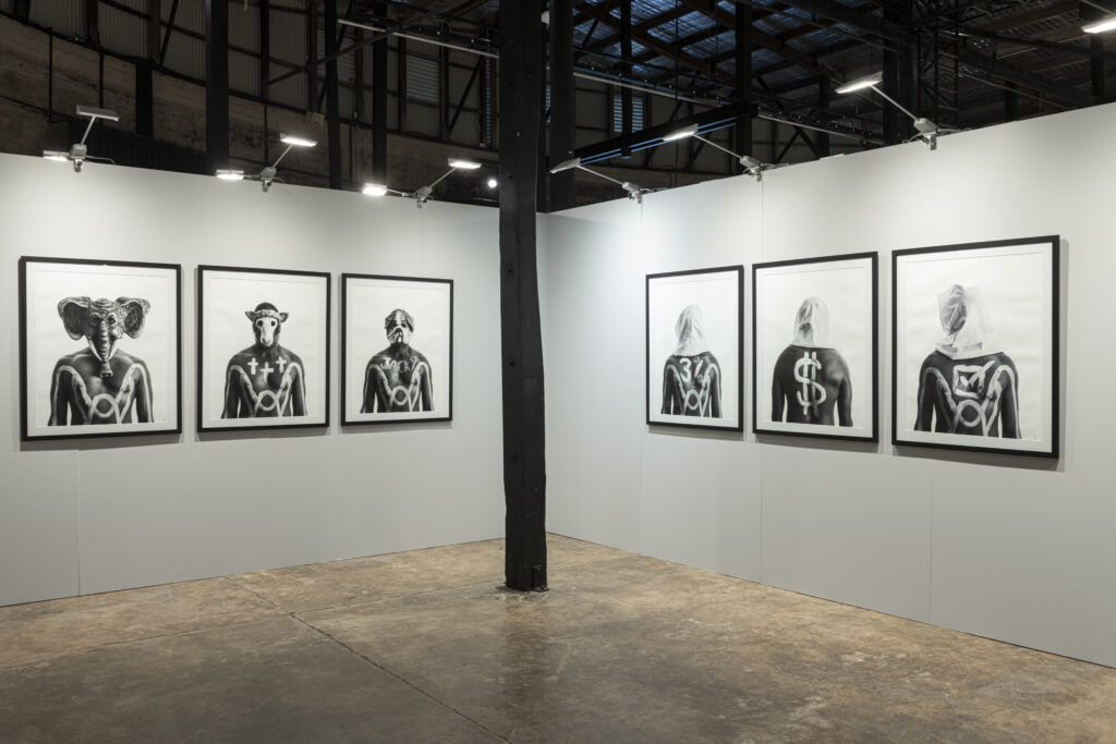An installation view of the exhibition. A series of black and white photographs are presented across two walls.