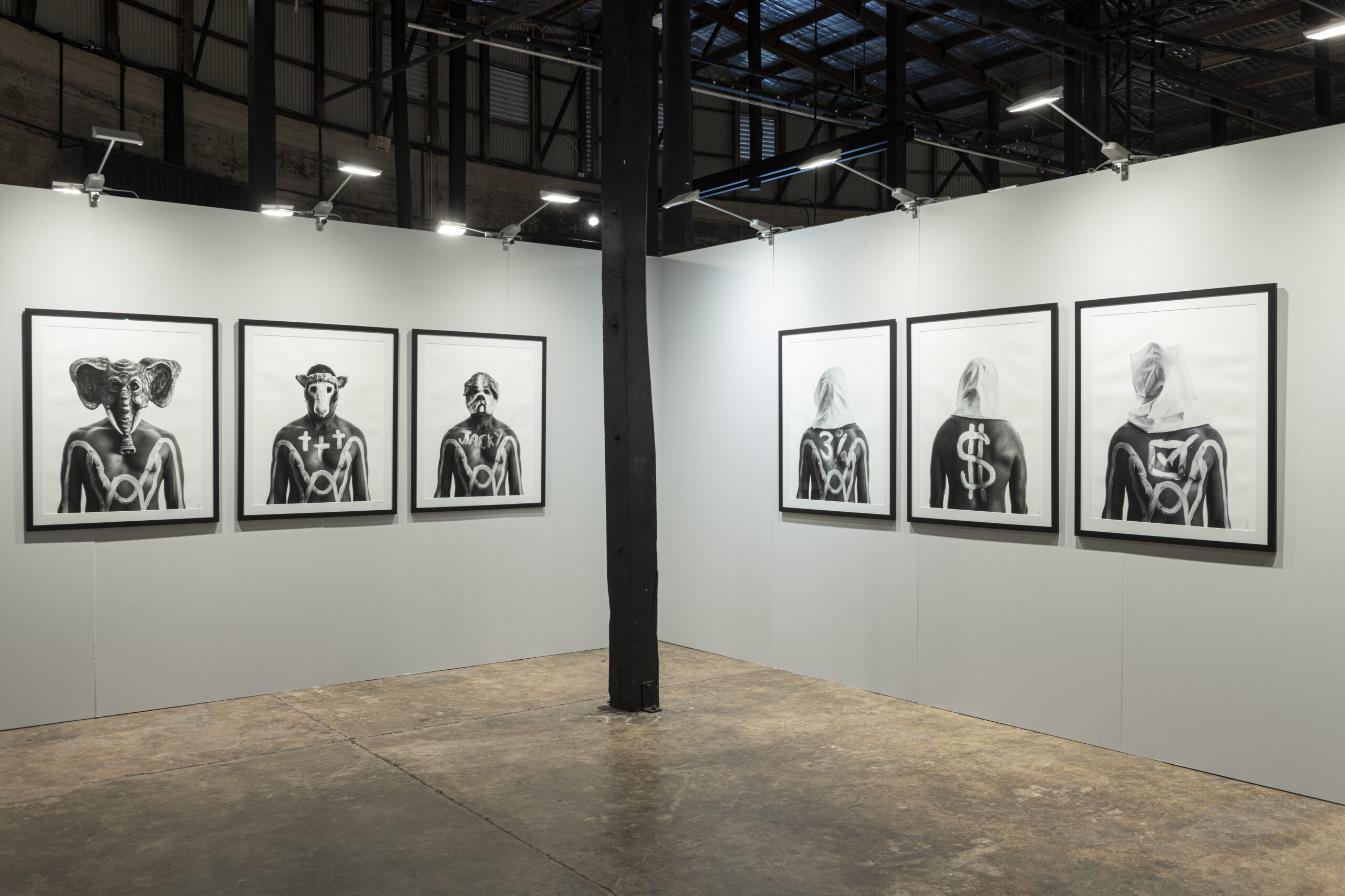 An installation view of the exhibition. A series of black and white photographs are presented across two walls.
