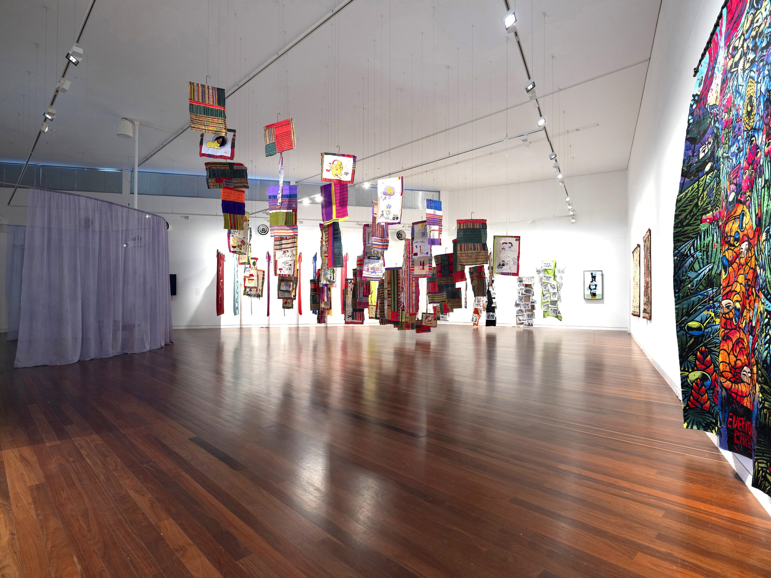 An array of textiles suspended from the ceiling in a mosaic-like arrangement.