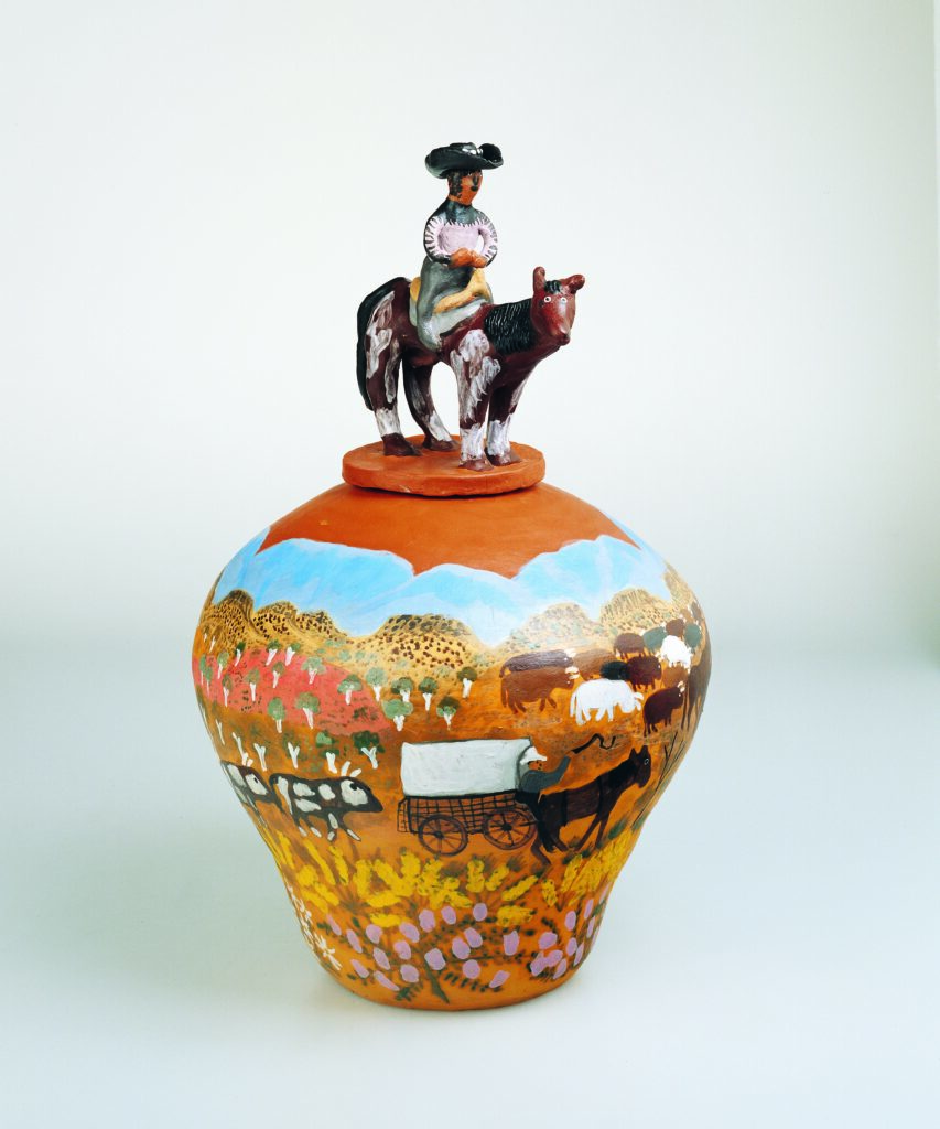 A terracotta pot decorated with a scene of drovers and cattle crossing terrain. The lid of the pot is a three-dimensional drover astride a horse. 