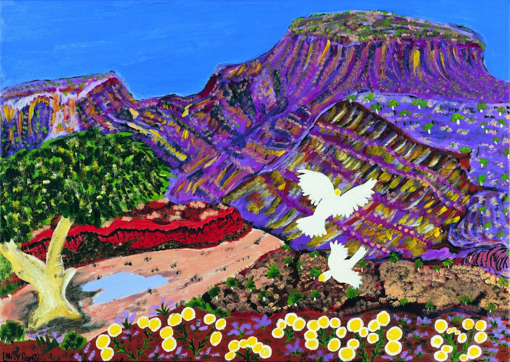A scene shows white crested cockatoos flying over purple mountains a valley containing a tree and a small body of water.