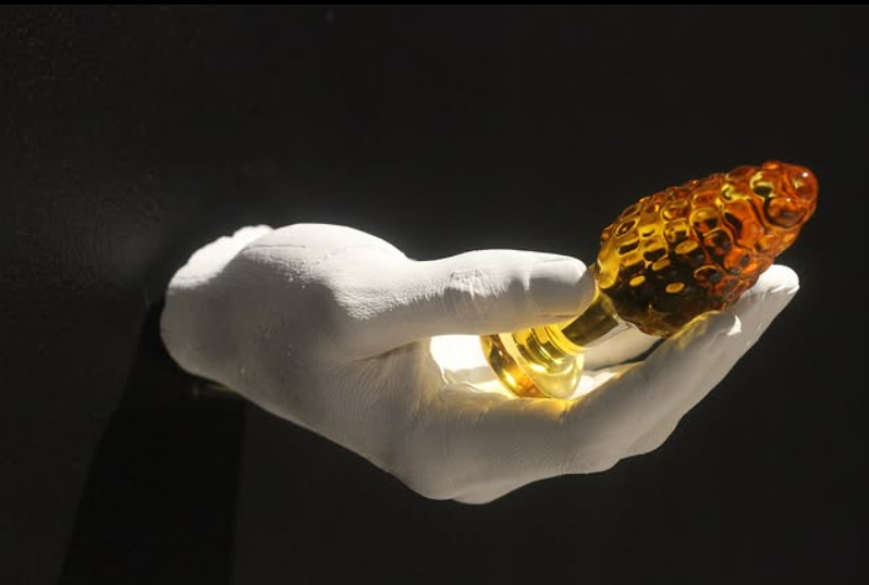 a white plaster hand protrudes from the wall holding a golden sex toy